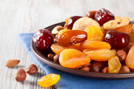 Dried fruits on a wooden background. Dates, lemon, apricots, figs and nuts in a clay plate. の写真素材