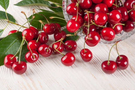 Scattered red sweet cherry and green leaves on a wooden backgroundの写真素材