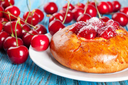 Fresh homemade bun with sweet cherry in a white dish on a blue wooden backgroundの写真素材