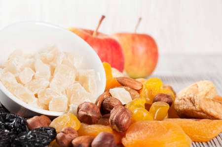 Pieces of dried pineapple, apricot, nuts and red apples on a wooden background. Various fruit snacks.の写真素材
