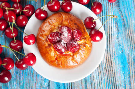 Fresh homemade bun with sweet cherry in a white dish on a blue wooden background. Top view.の写真素材