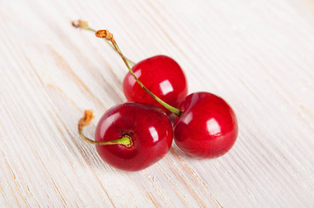 Three red sweet cherries on awooden background