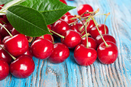 Red ripe sweet cherry and green leaves on a blue wooden backgroundの写真素材