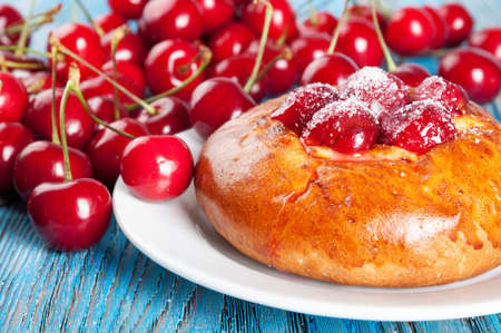 Fresh homemade bun with sweet cherry in a white dish on a blue wooden backgroundの写真素材