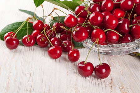 Scattered red sweet cherry and green leaves on a wooden backgroundの写真素材