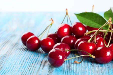 Red sweet cherry and green leaves on a blue wooden backgroundの写真素材
