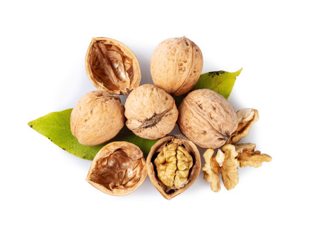Whole and cracked walnuts on a white background. Half of walnut, green leaves and shell. Top view