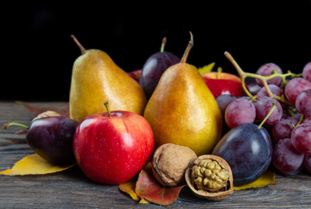 Autumn still life with walnuts, grape, pears and apple on a brown wooden table. Fruit and nuts on a black backgroundの写真素材