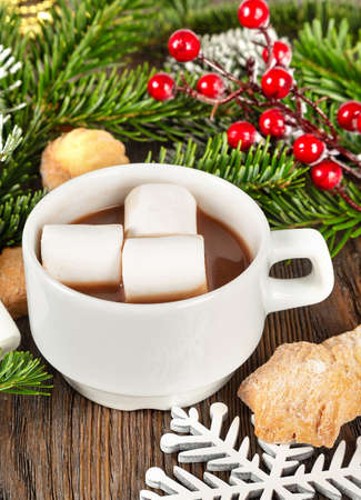 Hot chocolate or cocoa drink with marshmallow in a white cup, sweet homemade cookies and fir tree on a brown wooden background. Christmas and new year traditional food.の写真素材