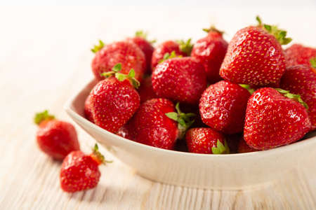 Fresh juicy ripe red strawberry in a white plate on a wooden backgroundの写真素材