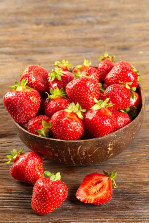 Fresh juicy ripe red strawberry in a coconut plate on a brown wooden background.の写真素材
