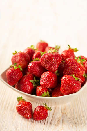 Fresh juicy ripe red strawberry in a white plate on a wooden backgroundの写真素材