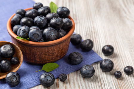 Fresh blueberries in a brown plate and blue textile napkin on a wooden background.の写真素材