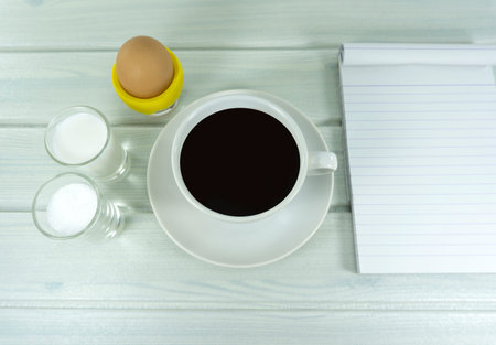 Hot coffee in the morning with milk in glass and Soft-boiled egg in cup on a white wooden floor...