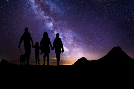 Night time long exposure landscape photography. A family with a dog on a high place looking amazed at the Milky Way, composite photoの写真素材