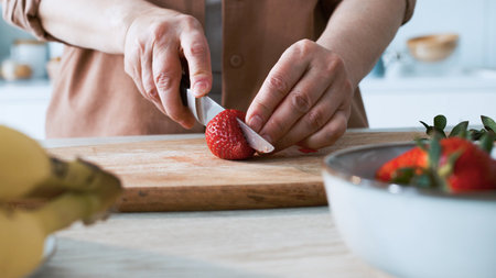 strawberries are cut into pieces on a wooden cutting board to decorate desserts. natural fresh fruits and berries for decorating cakes and cupcakes. recipes for cooking at home.の写真素材