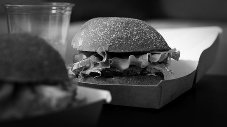 burger with tomatoes lettuce and pickles on a wooden plate and fries at the backの写真素材