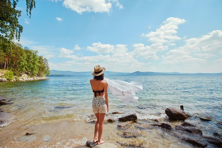 A slender woman in a white shirt and hat relaxes near the water.の写真素材
