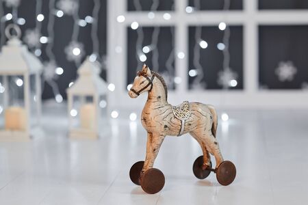 Toy wooden horse on wheels on the background of lights garland on a white wooden floorの写真素材