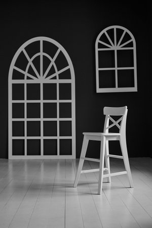 White chair on dark background. The wall is decorated with details in the form of arched doors and...