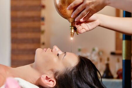 Shirodhara, an Ayurvedic healing technique. Oil dripping on the female forehead. Portrait of a young woman at an ayurvedic massage session with aromatic oil dripping on her forehead and hair.の写真素材