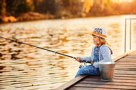 lonely little child fishing from wooden dock on lakeの写真素材