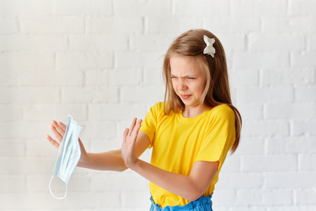 A little girl takes off her annoying protective sterile medical mask on a light background. Happy ending. Victory over the coronavirus. Pandemic Covid-19の写真素材