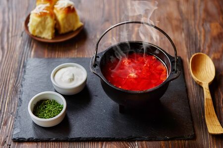 Traditional Ukrainian Russian vegetable borscht on an old wooden background in portioned cast iron. With herbs, sour cream and garlic bread.の写真素材