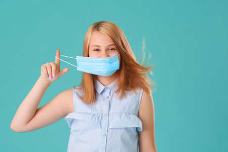 A young girl takes off her mask on a turquoise background, she is smiling and happy-she is tired of wearing a medical protective mask. Coronavirus pandemic. Quarantine. covid-19の写真素材