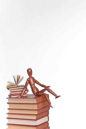 A wooden man sits on a stack of booksの写真素材