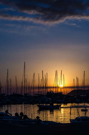 boats in the harbor at sunset with orange sky and dark cloudsの写真素材