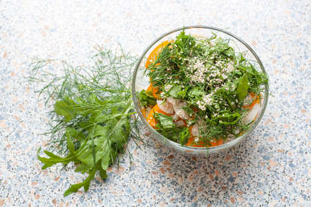 Salad of fresh yellow tomatoes and cucumber with herbs and sesame seeds in a glass bowl on a tableの写真素材