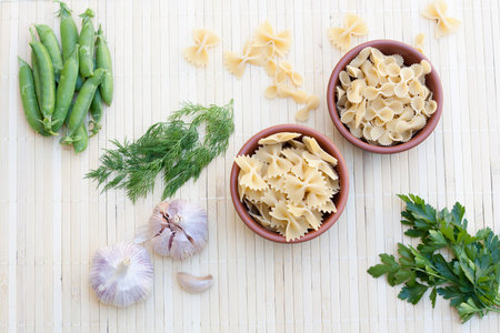 Pasta in a clay pot green peas herbs and spices on light makisu