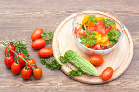 Salad of fresh yellow and pink tomatoes and cucumber with parsley in a glass bowl on a wooden tableの写真素材