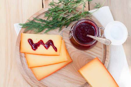 Sliced cheese and cherry sauce on a wooden board with dill and rosemaryの写真素材
