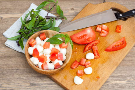 Sliced tomatoes, basil and mozzarella cheese on a wooden plate の写真素材
