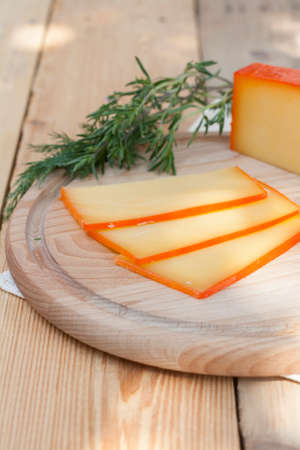 Sliced cheese on wooden board with dill and rosemary, selective focusの写真素材