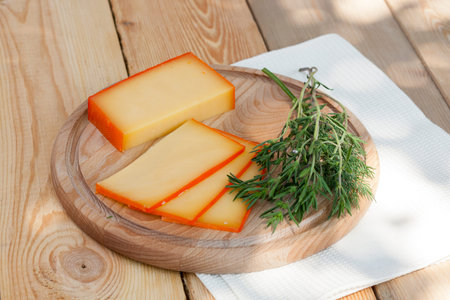Sliced cheese on wooden board with dill and rosemary, selective focus