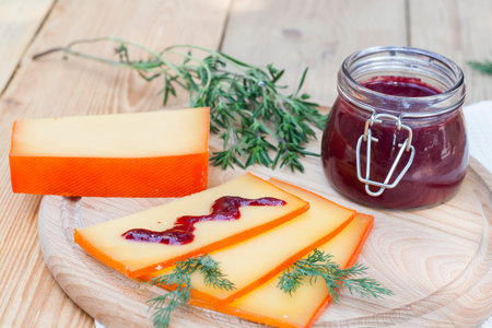 Sliced cheese and cherry sauce on a wooden board with dill and rosemary