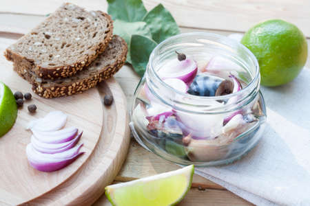 Slices of marinated mackerel with onion in a jar, lime, laurel and bread on wooden board, selective focusの写真素材