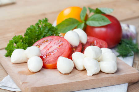 Sliced tomatoes, basil and mozzarella cheese on a wooden board, selective focusの写真素材