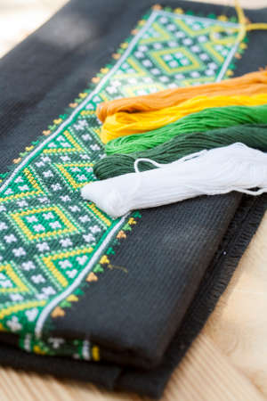 Ukrainian embroidery on the black fabric and thread embroidery on a light wooden table, selective focusの写真素材