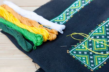 Ukrainian embroidery on the black fabric and thread embroidery on a light wooden table, selective focusの写真素材