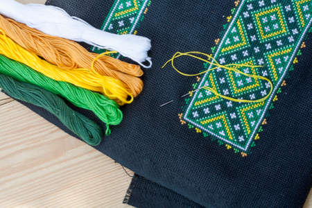 Ukrainian embroidery on the black fabric and thread embroidery on a light wooden table, selective focusの写真素材