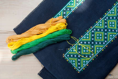 Ukrainian embroidery on the black fabric and thread embroidery on a light wooden table, selective focusの写真素材