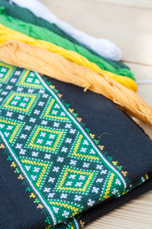 Ukrainian embroidery on the black fabric and thread embroidery on a light wooden table, selective...