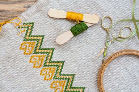 Ukrainian embroidery on the linen fabric and thread embroidery on a wooden table, selective focusの写真素材
