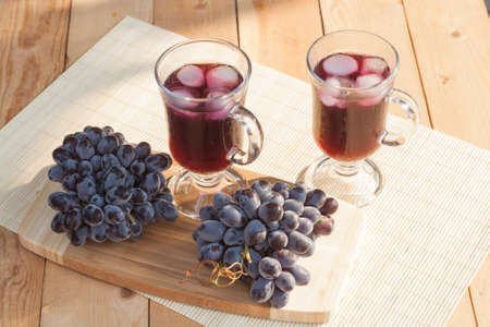 Grape juice cooler with ice in glass and glass of fresh blue grapes on a wooden table close-up, selective focusの写真素材