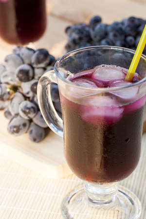 Grape juice cooler with ice in glass and glass of fresh blue grapes on a wooden table close-up, selective focusの写真素材