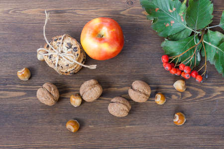 Apple, cookies with chocolate, nuts, mountain ash and red autumn leaves on a wooden tableの写真素材